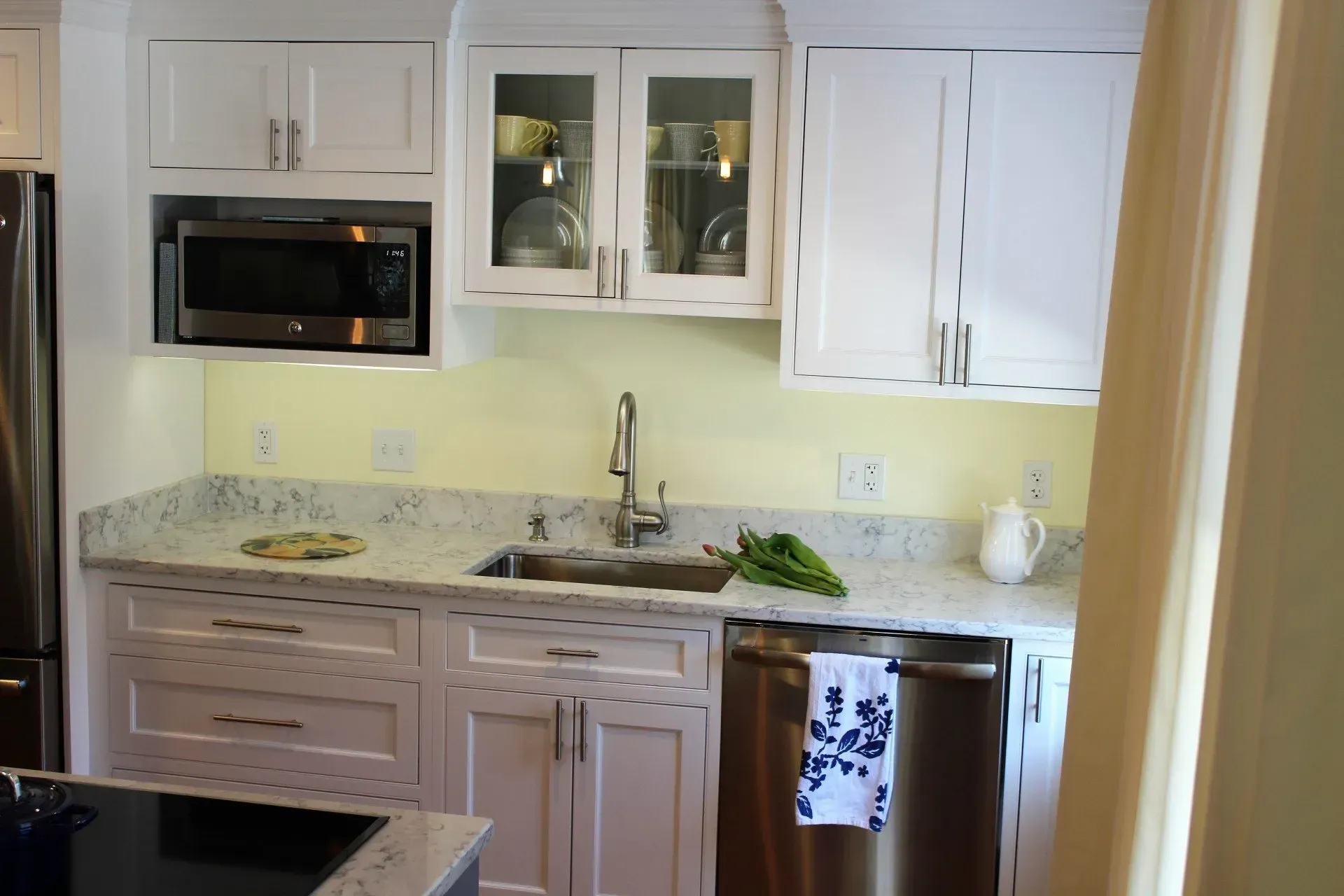 White kitchen with granite countertops, stainless steel appliances, and glass-door cabinets.