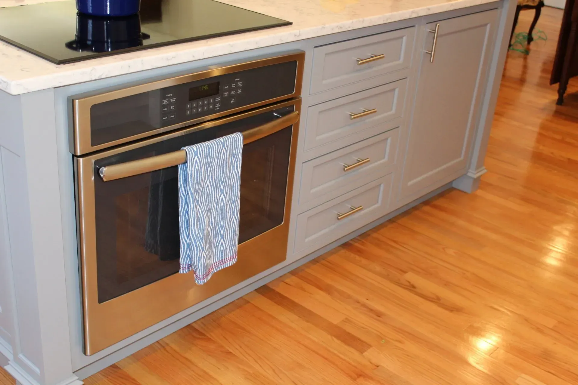 Built-in oven with blue and white towel in a gray kitchen island with wood flooring.