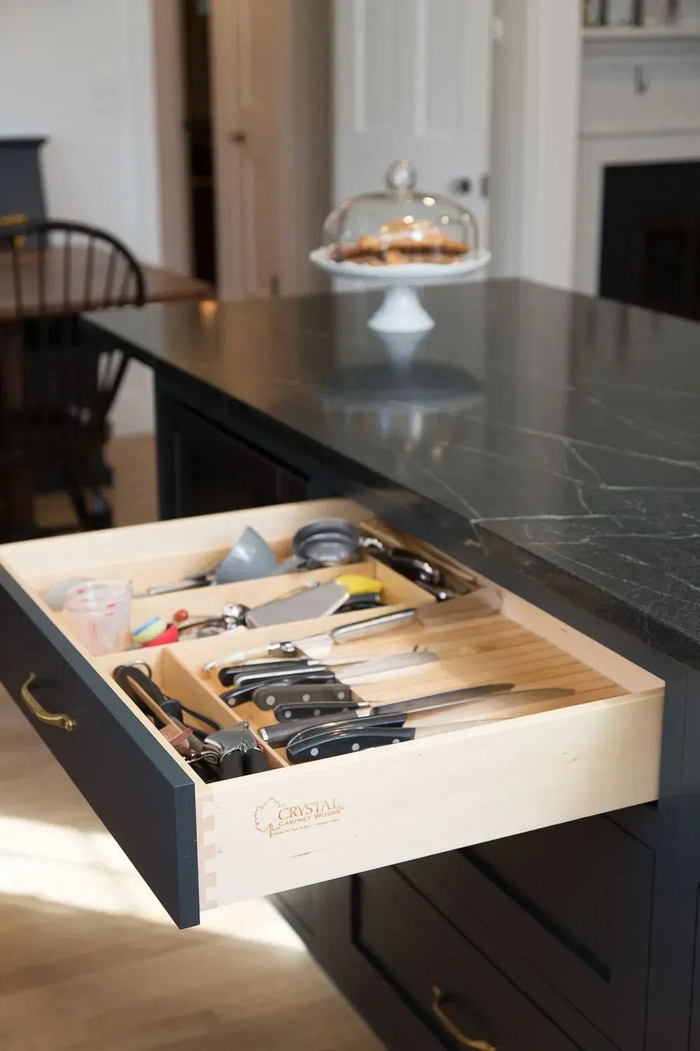 Kitchen island with open drawer revealing organized utensils. Black countertop, light wood drawer interior.