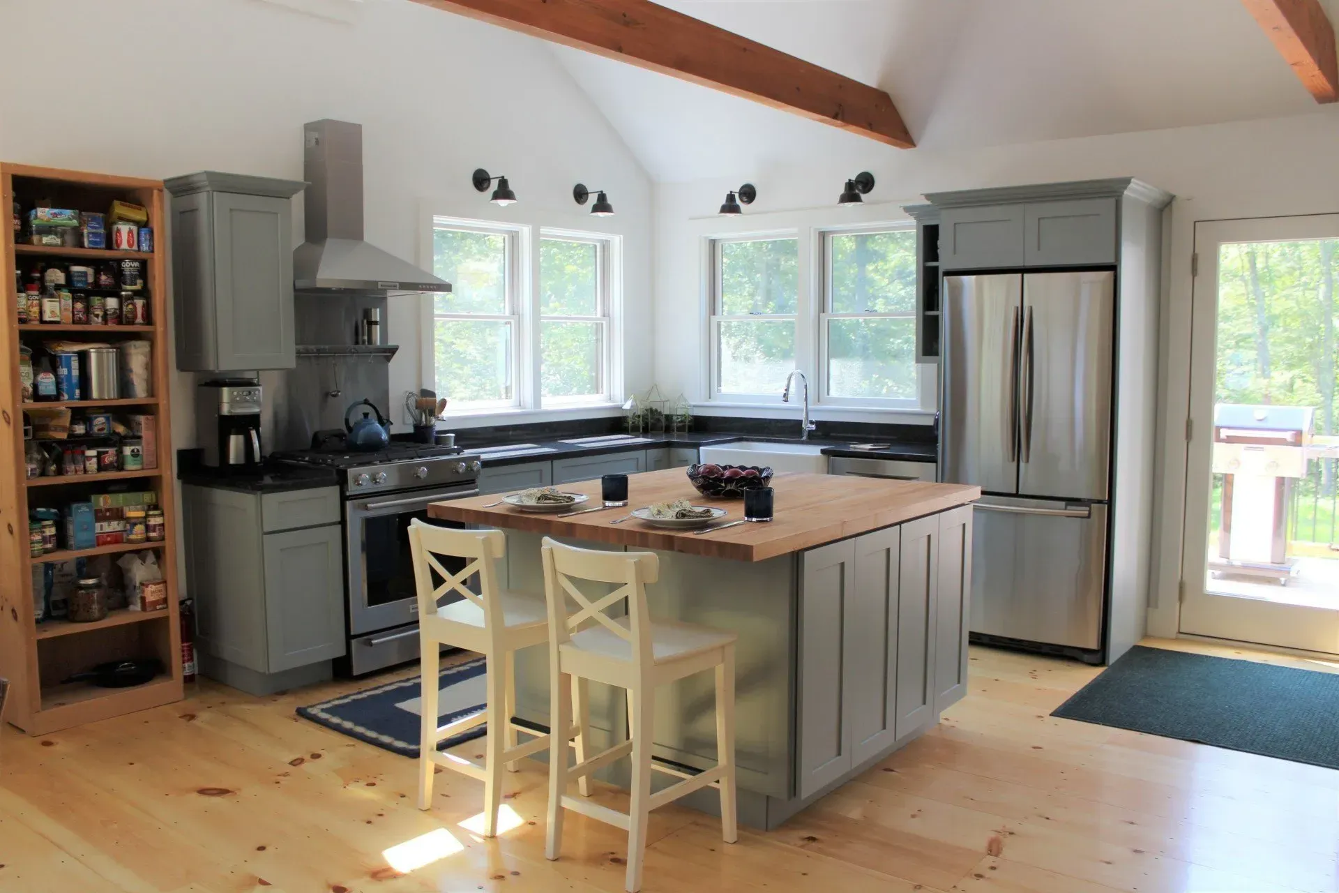 Kitchen with gray cabinets, stainless steel appliances, and island with two chairs.