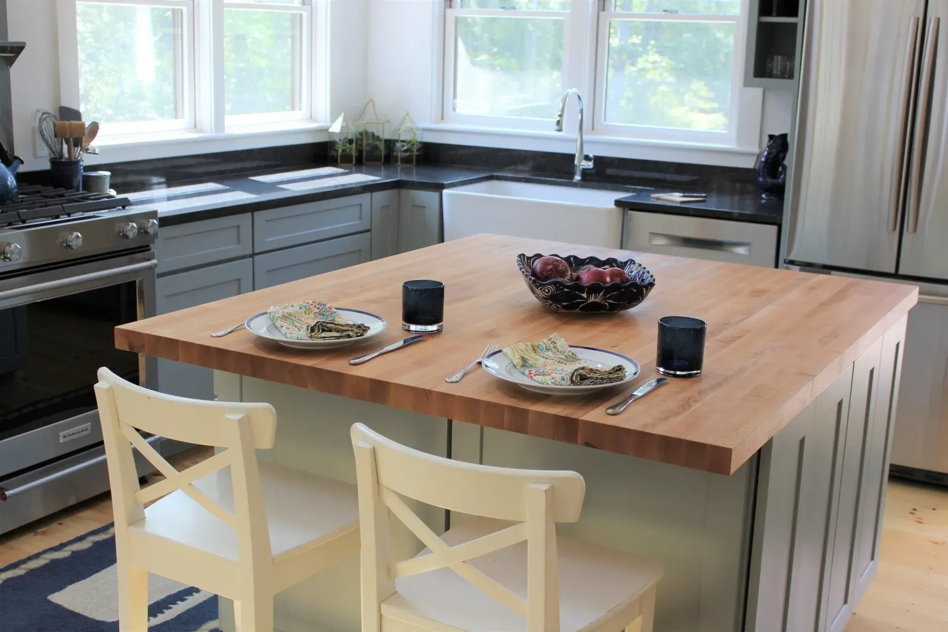 Kitchen with light-colored island, chairs, and countertops. Table settings, food, and berries are on the island.