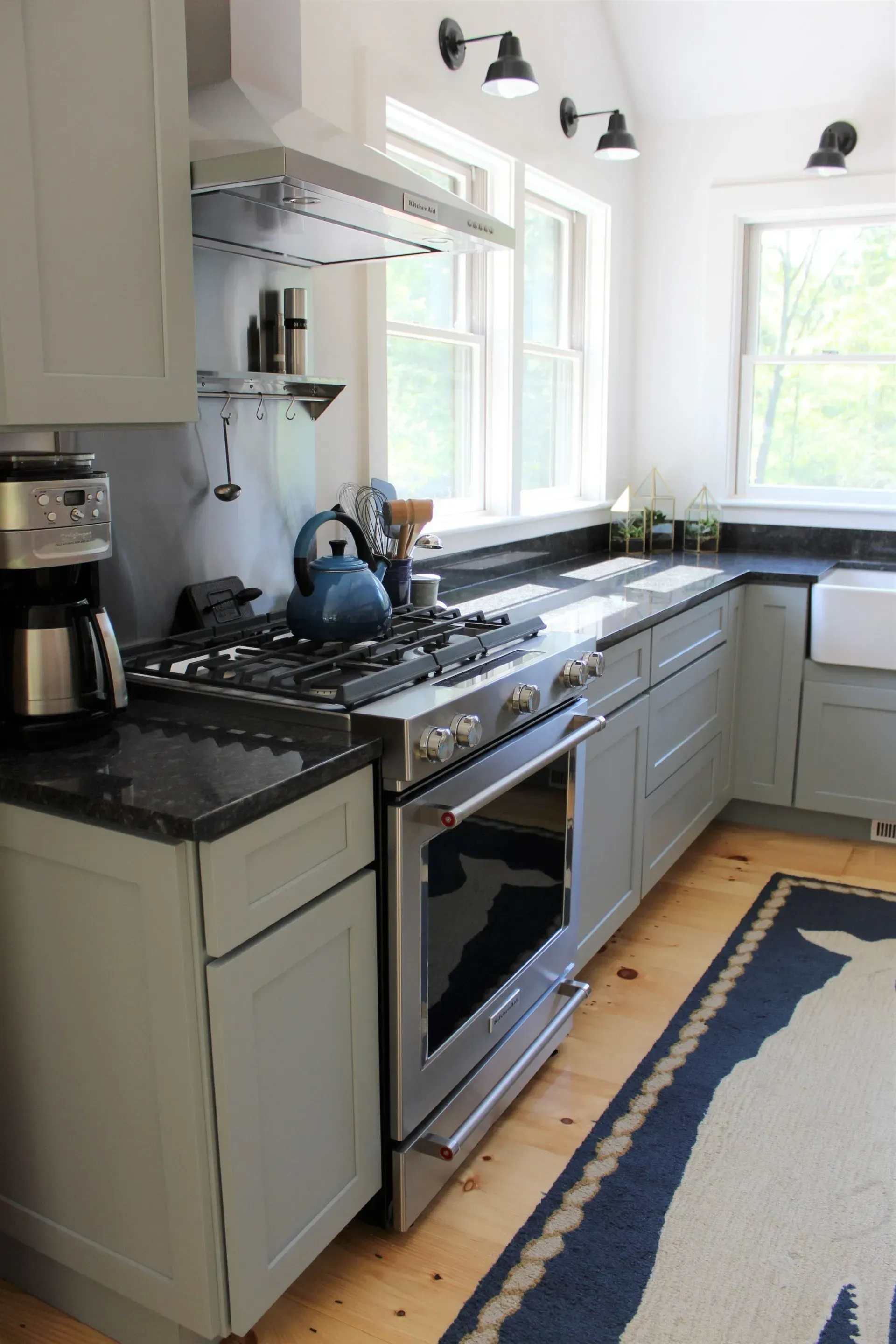 Kitchen with gray cabinets, black countertops, stainless steel oven, and blue kettle.