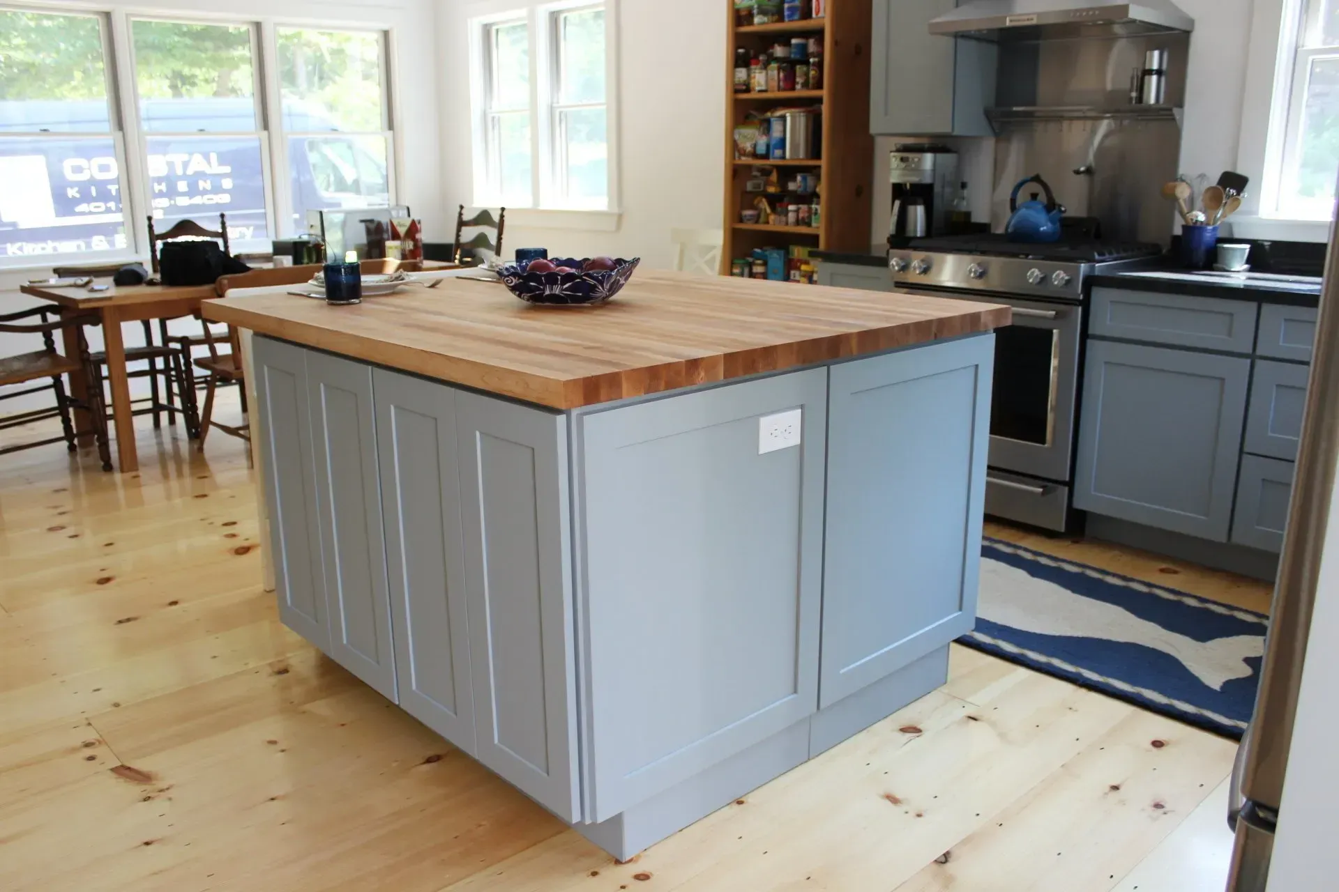 Kitchen with light wood floor, gray island, wooden countertop, and dark gray cabinets.