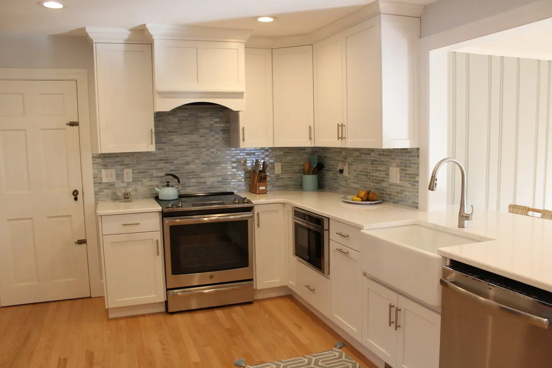White kitchen with stainless steel appliances, light-colored countertops, and blue-tiled backsplash.