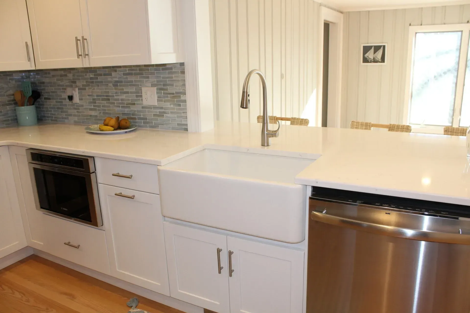 White kitchen with farmhouse sink, stainless steel appliances, blue tile backsplash, and light wood floors.