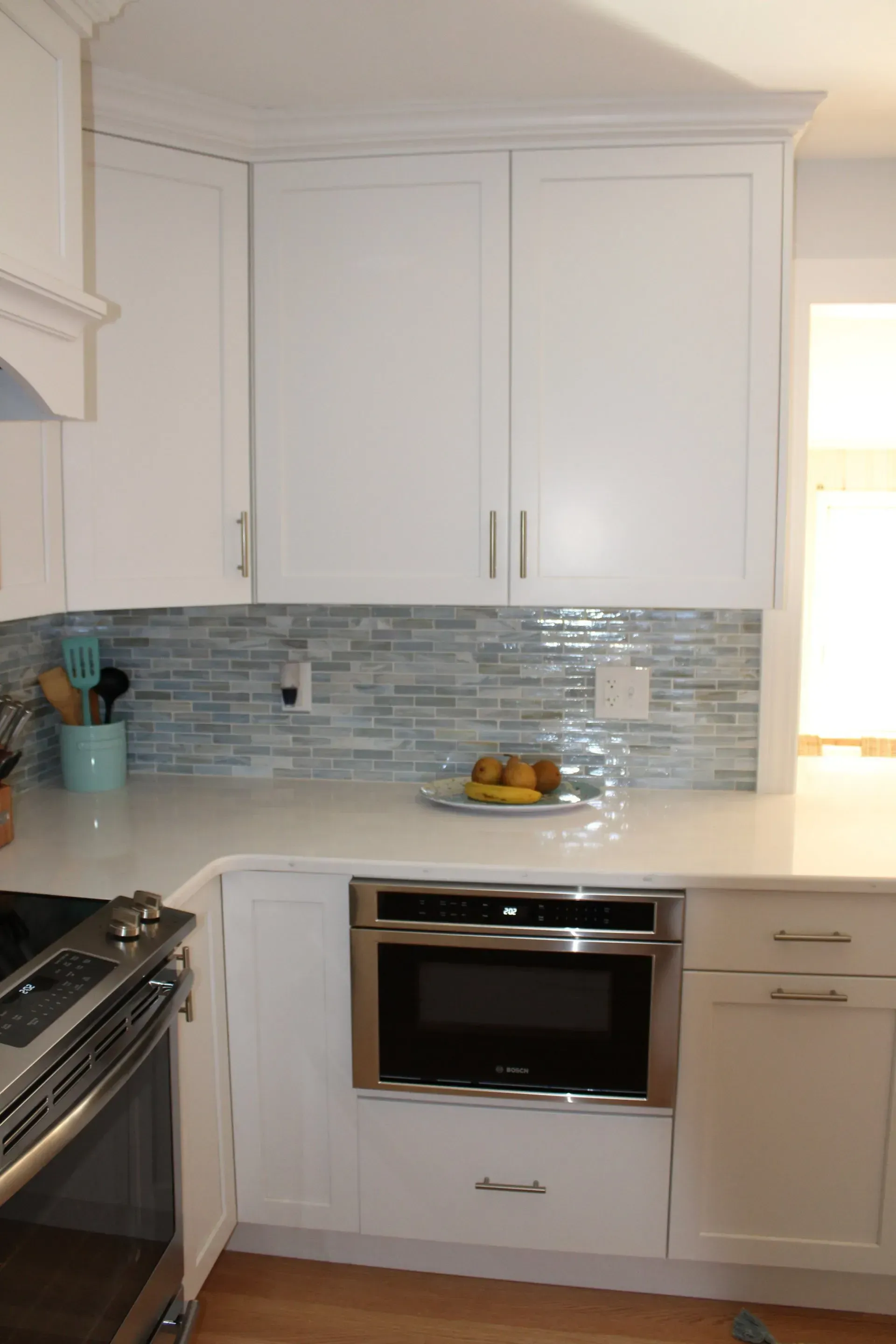 White kitchen with blue tiled backsplash, built-in microwave, white cabinets, and stainless steel range.