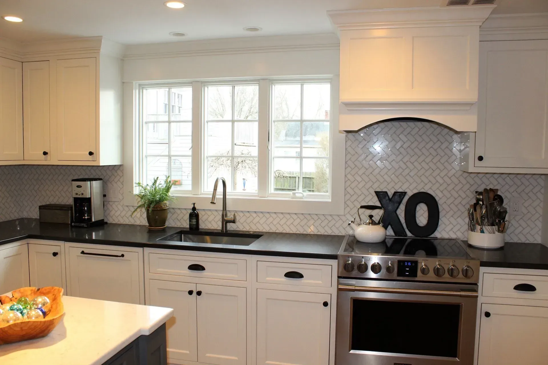 White kitchen with black countertops, stainless steel appliances, and a window above the sink.