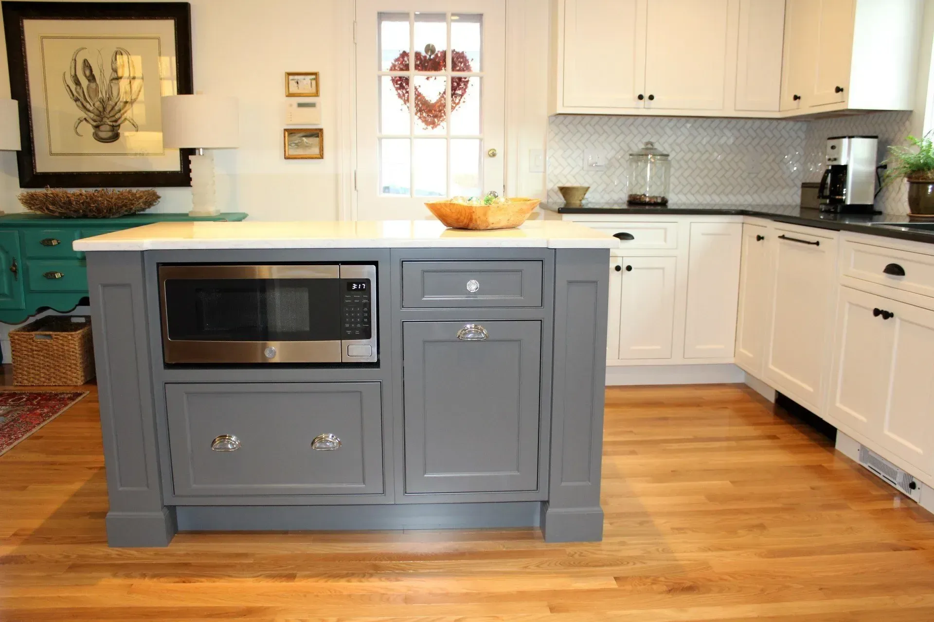Kitchen with gray island housing microwave, white cabinets, and wood flooring.