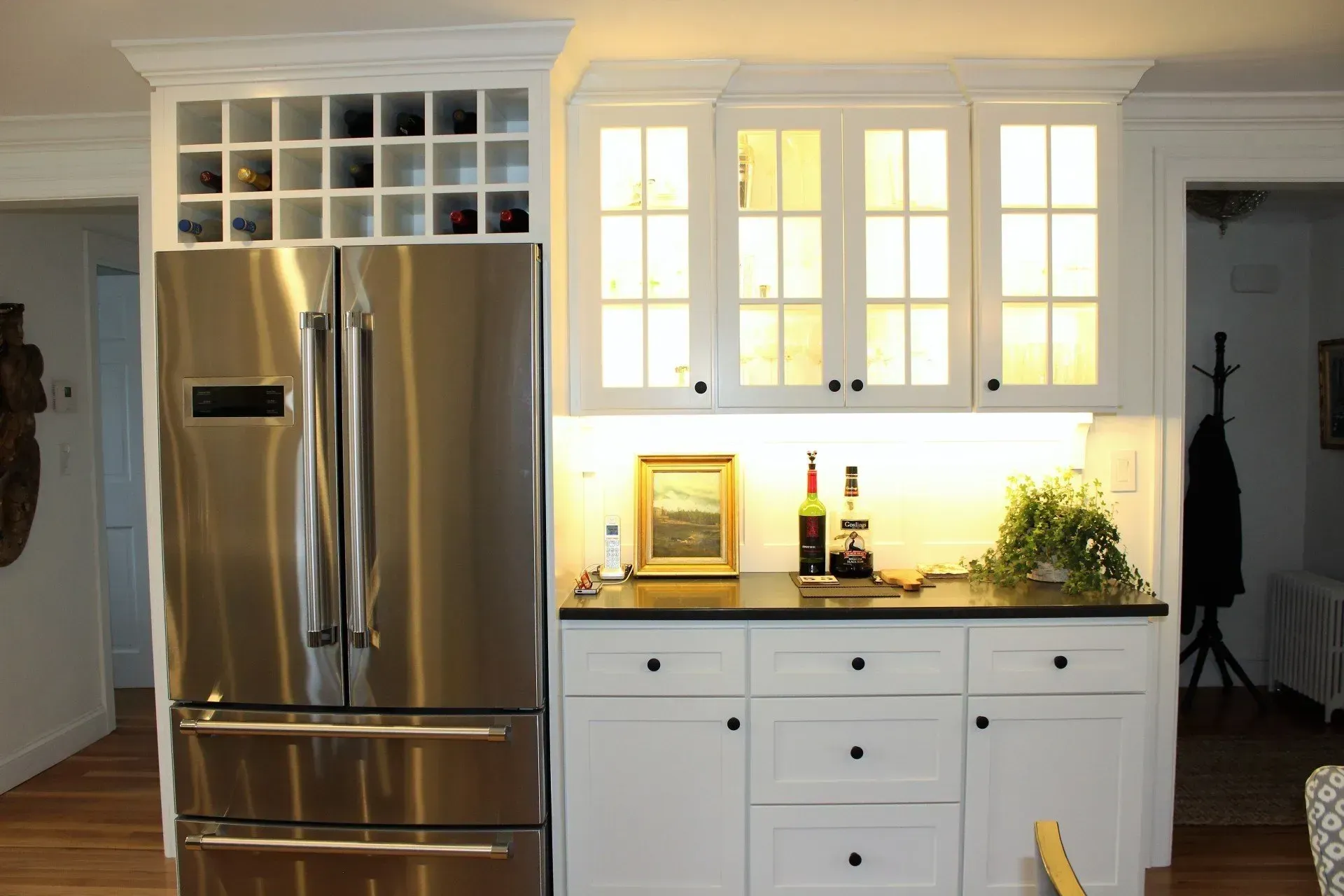 Stainless steel refrigerator next to white cabinets with wine storage and illuminated display.