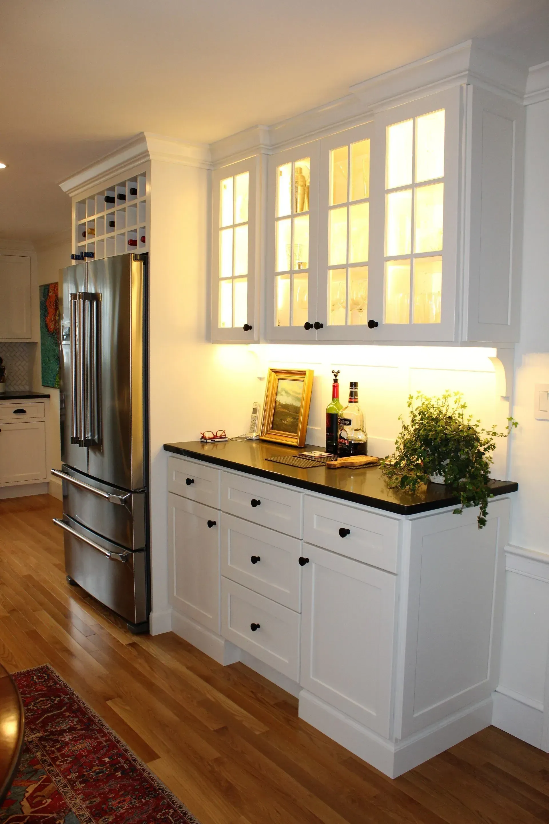White kitchen cabinetry with black countertop, stainless steel refrigerator, and hardwood flooring.