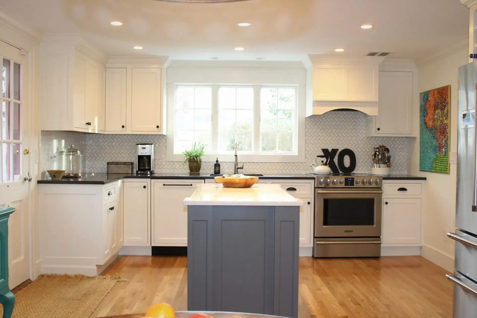 White kitchen with gray island, black countertops, and wooden floors.