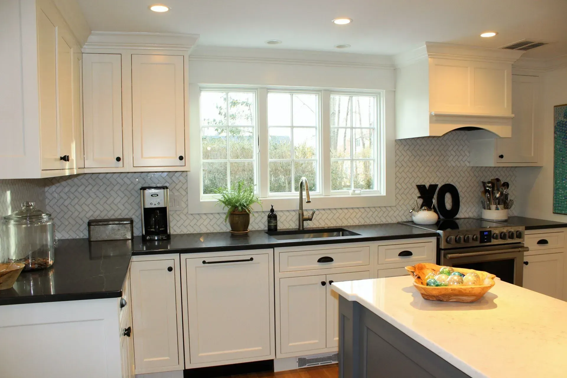 White kitchen with black countertops, a window, and a gray island.