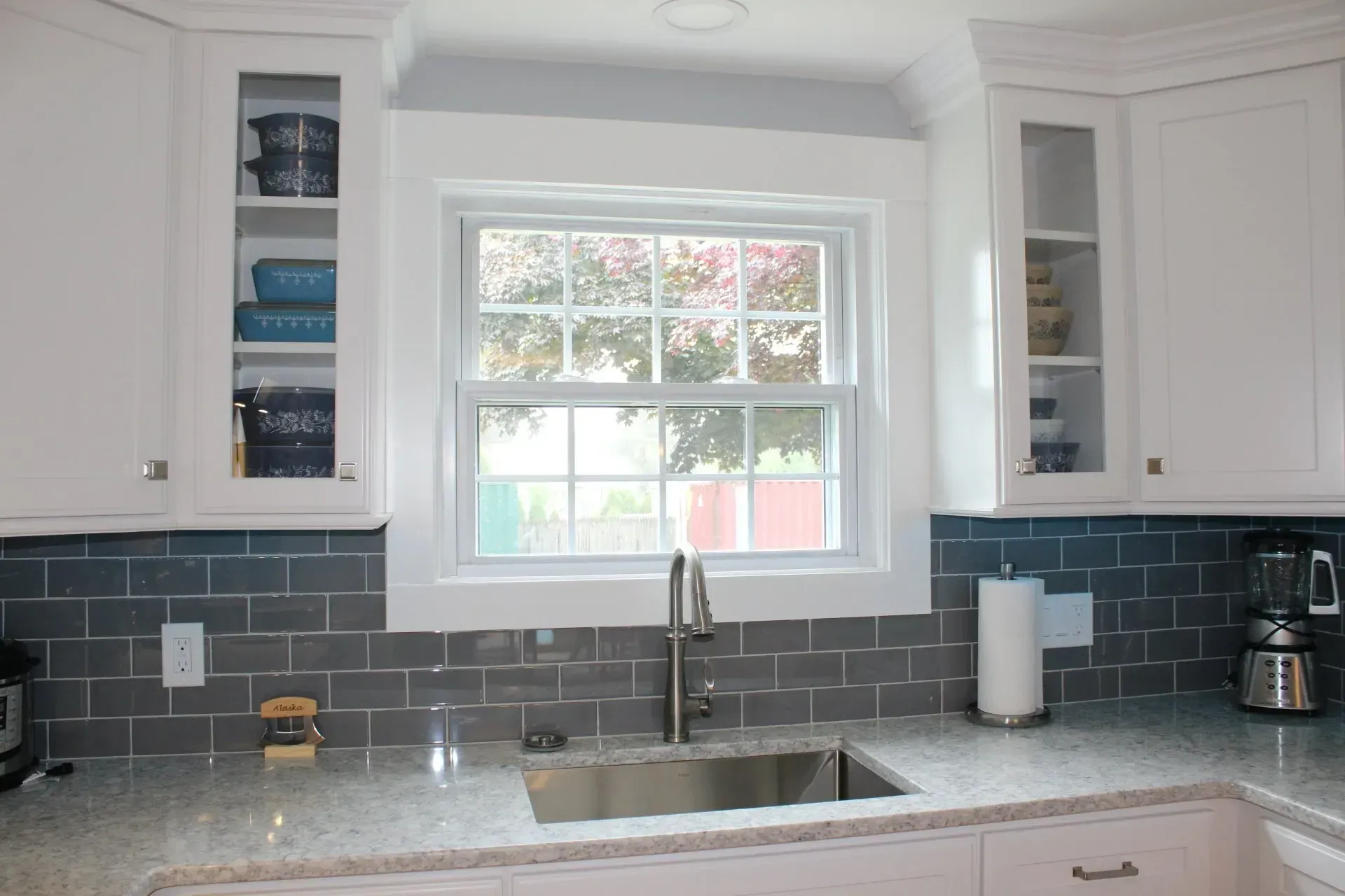 Kitchen with white cabinets, gray backsplash, window above the sink, granite countertop.