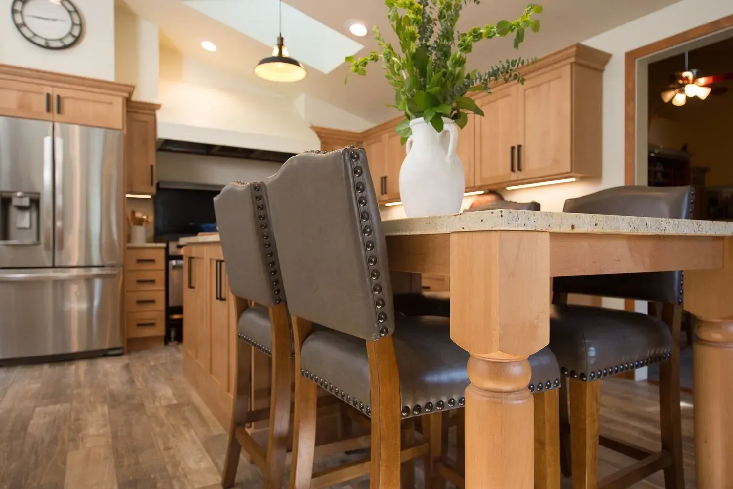 Kitchen with light wood cabinets, stainless steel refrigerator, and a center island with bar stools.