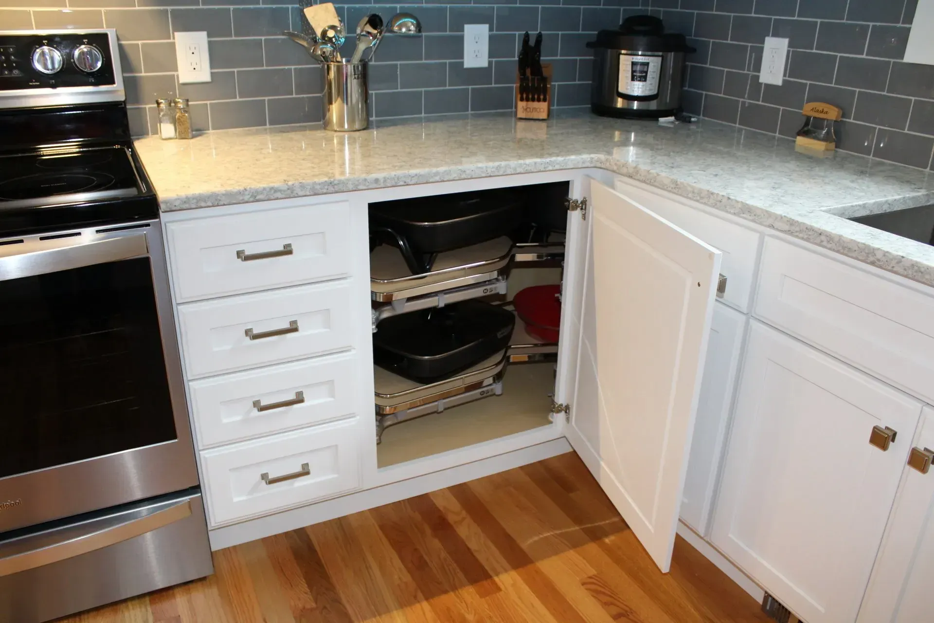 White kitchen cabinets with open corner door revealing stored cookware, granite countertop, and gray tiled backsplash.
