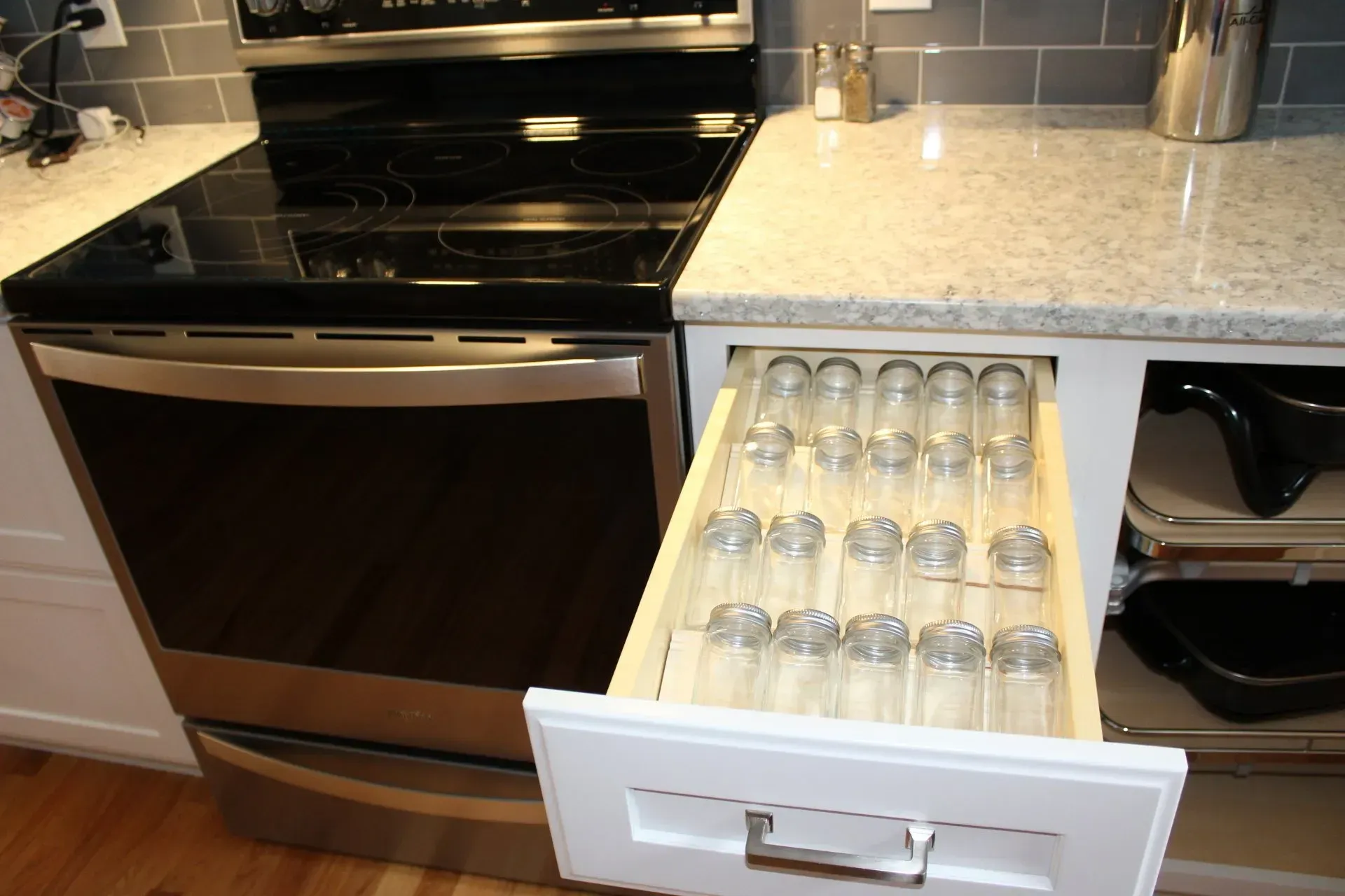 Kitchen cabinet drawer open with spice jars next to the oven.