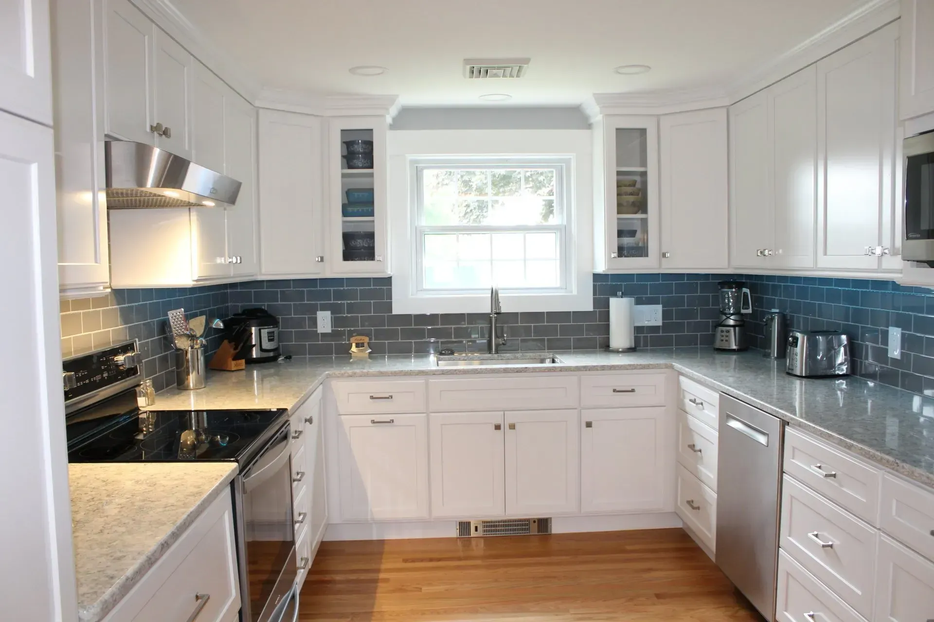 White U-shaped kitchen with blue tiled backsplash, stainless steel appliances, and wood floor.