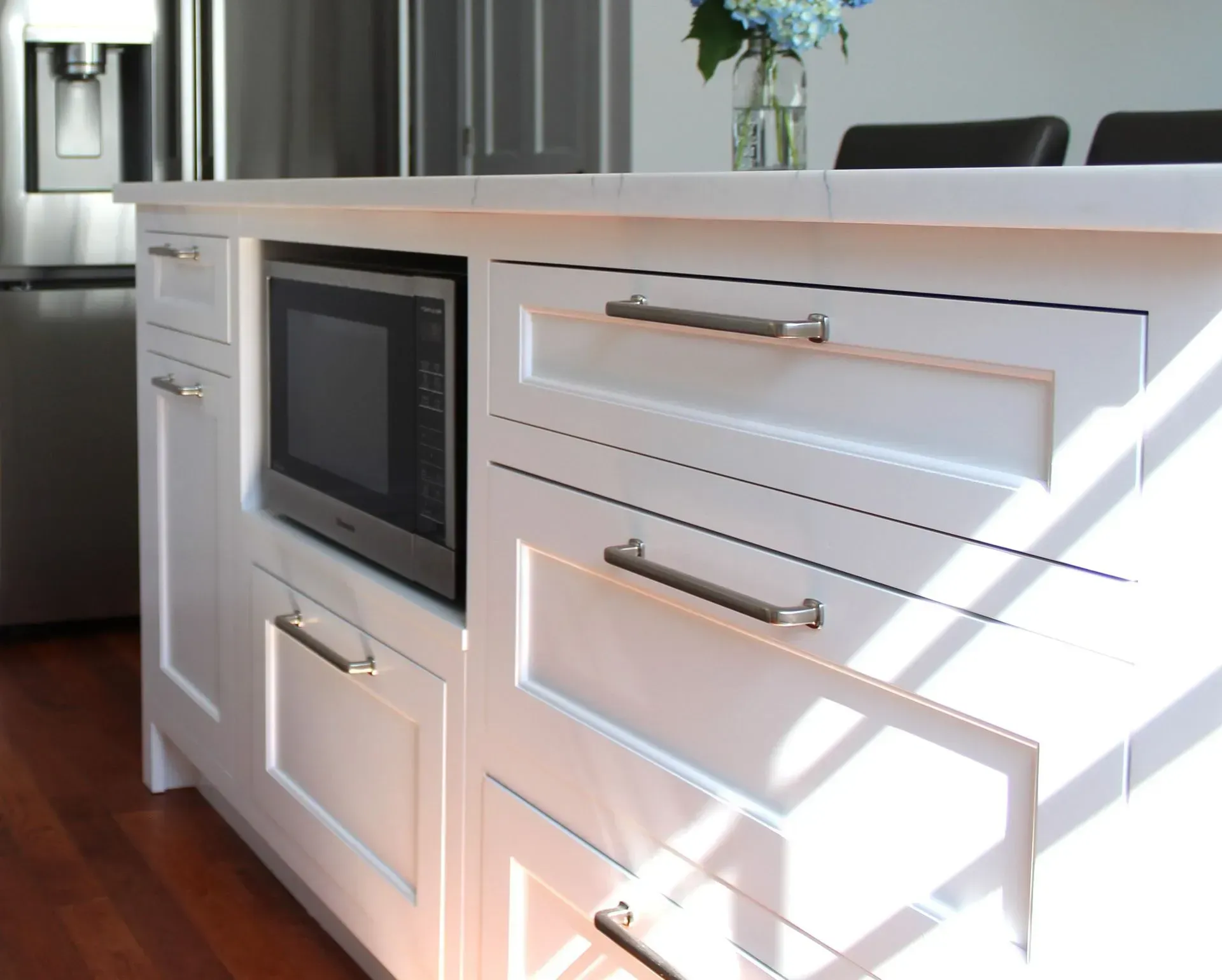 White kitchen island with a microwave, drawers, and metallic handles.