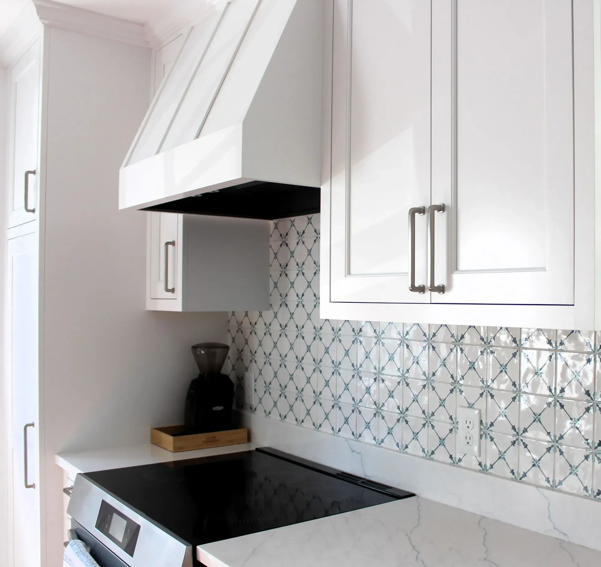 White kitchen with stove, range hood, and patterned blue and white tile backsplash.