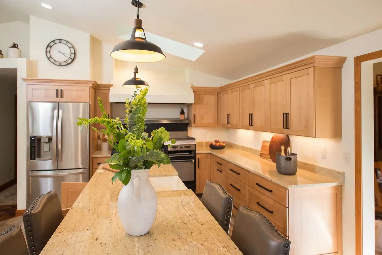Kitchen with light wood cabinets, stainless steel appliances, and a long island with a white vase of greenery.