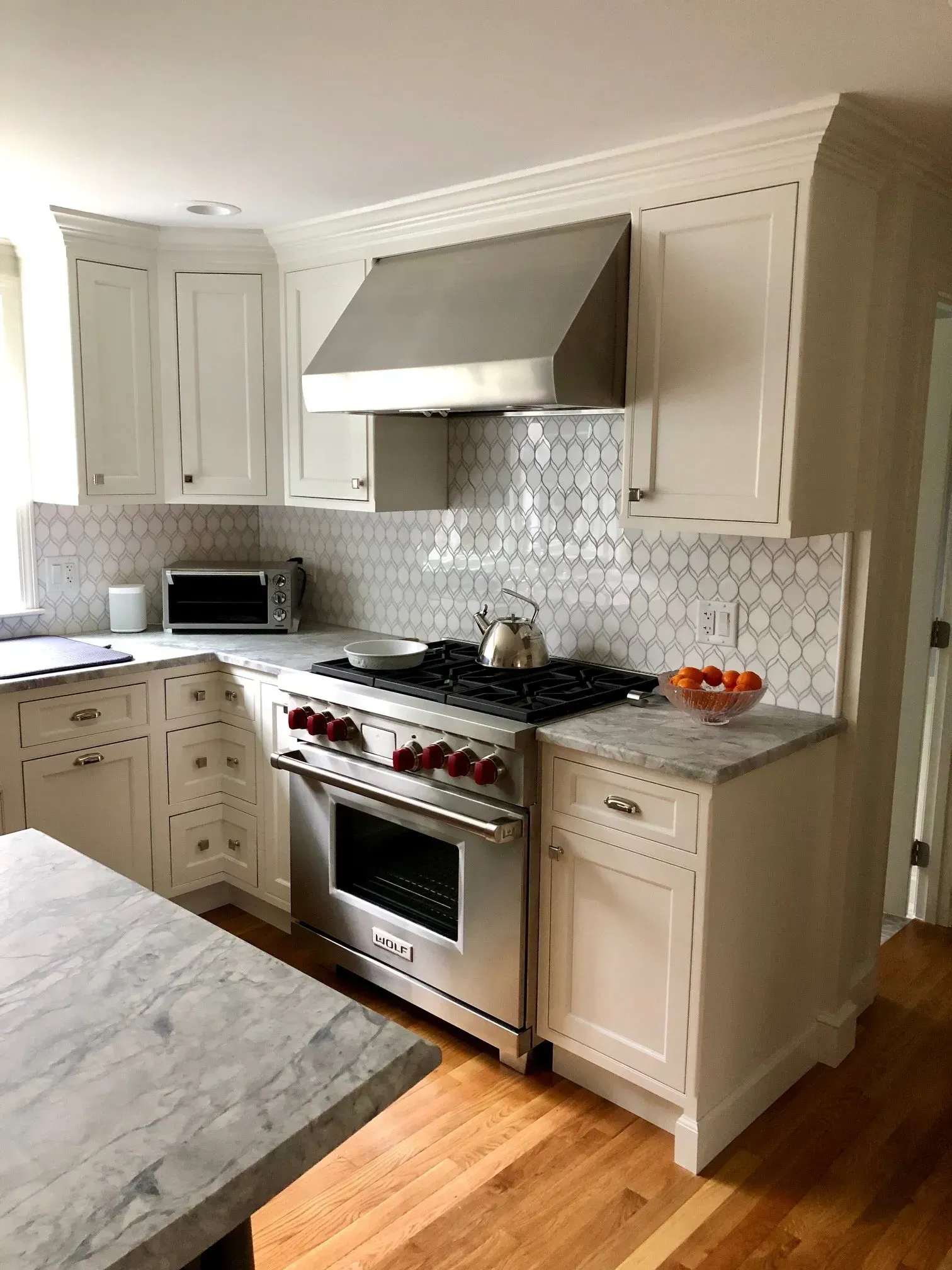 White kitchen with stainless steel oven, hood, and light-colored countertops.