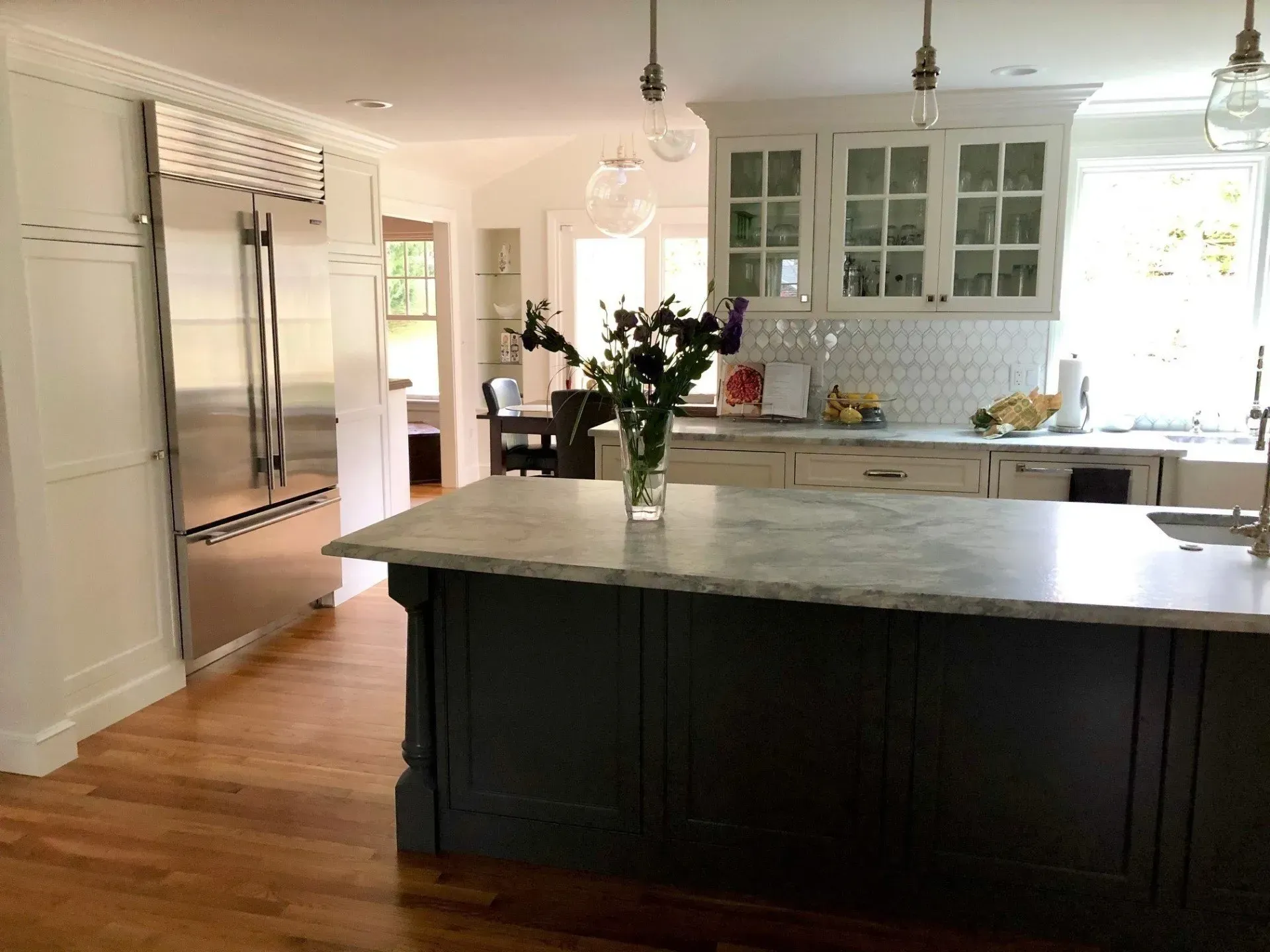 Spacious kitchen with a dark blue island, white cabinets, stainless steel refrigerator, and hardwood floors.