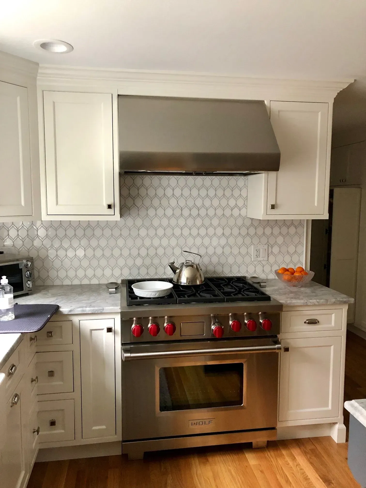 Kitchen with stainless steel stove, hood, and white cabinets. White tile backsplash, light counter, and wooden floor.