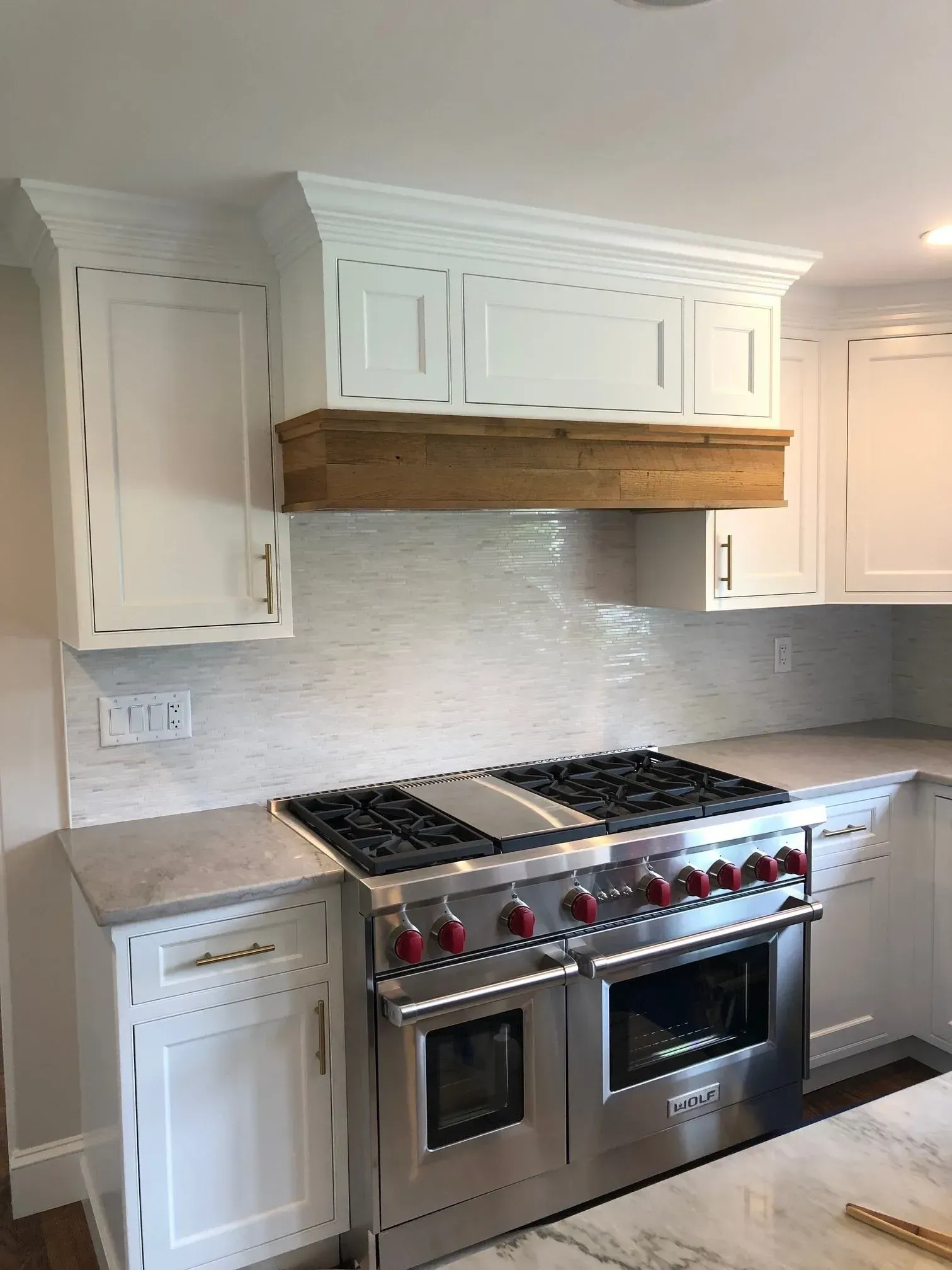 Kitchen with white cabinets, stainless steel stove, and wooden range hood.