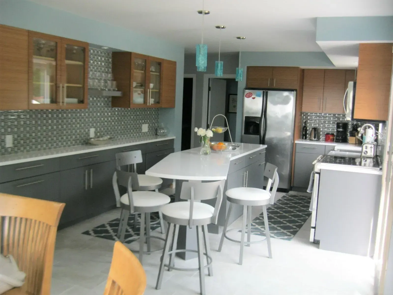 Modern kitchen with gray cabinets, white countertops, and wood accents; island with seating.