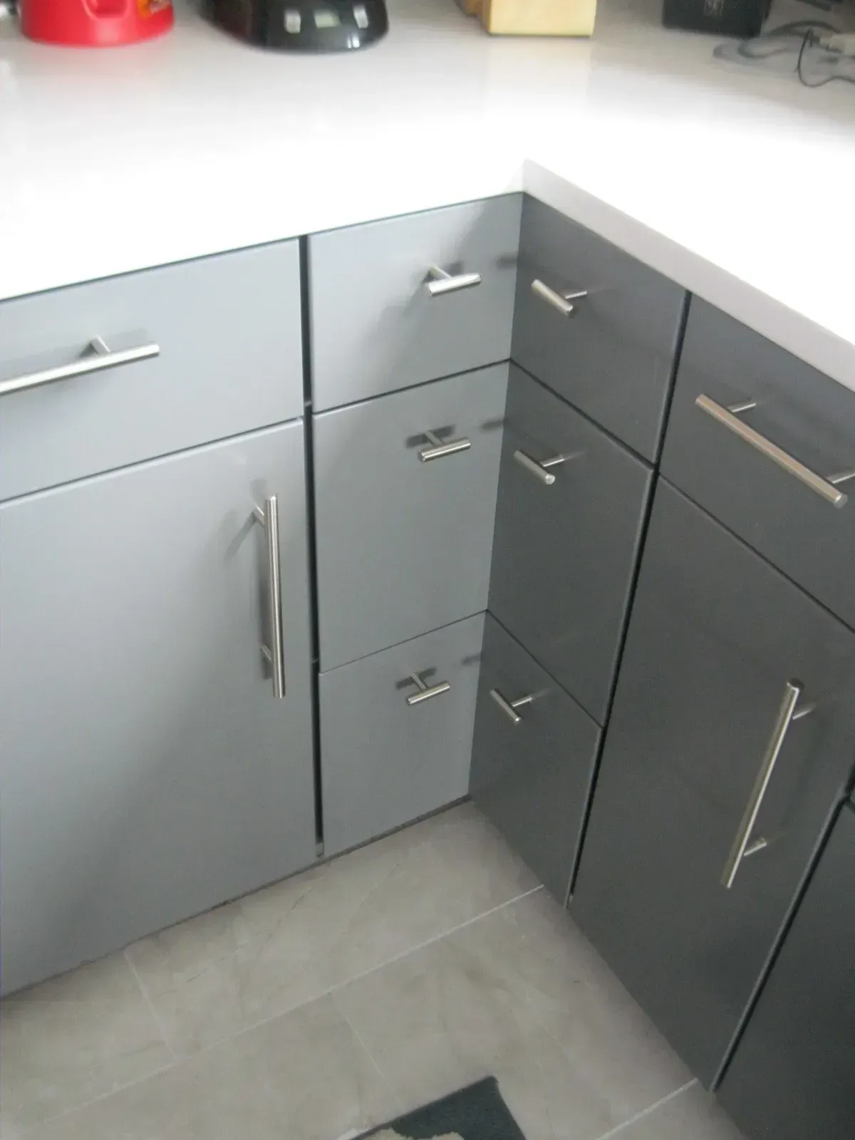 Gray kitchen cabinets with silver handles under a white countertop.