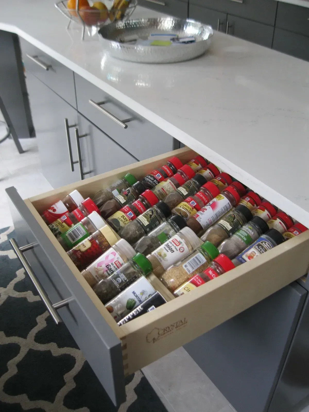 Open kitchen drawer filled with labeled spice bottles, gray cabinet, white countertop.