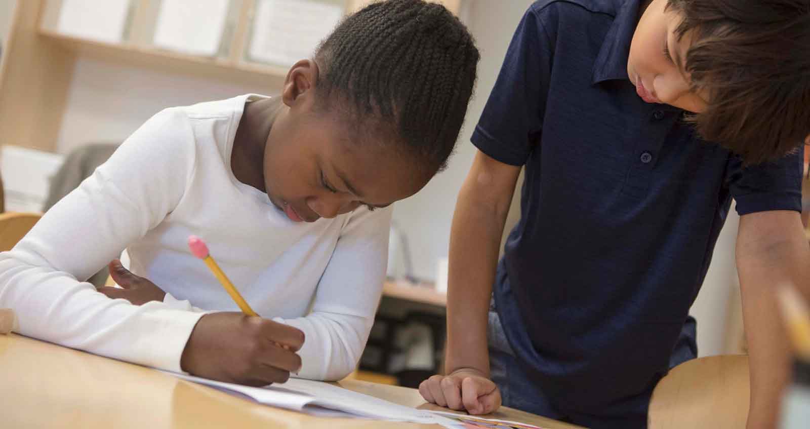 A little girl is using a pencil and paper to complete a school task