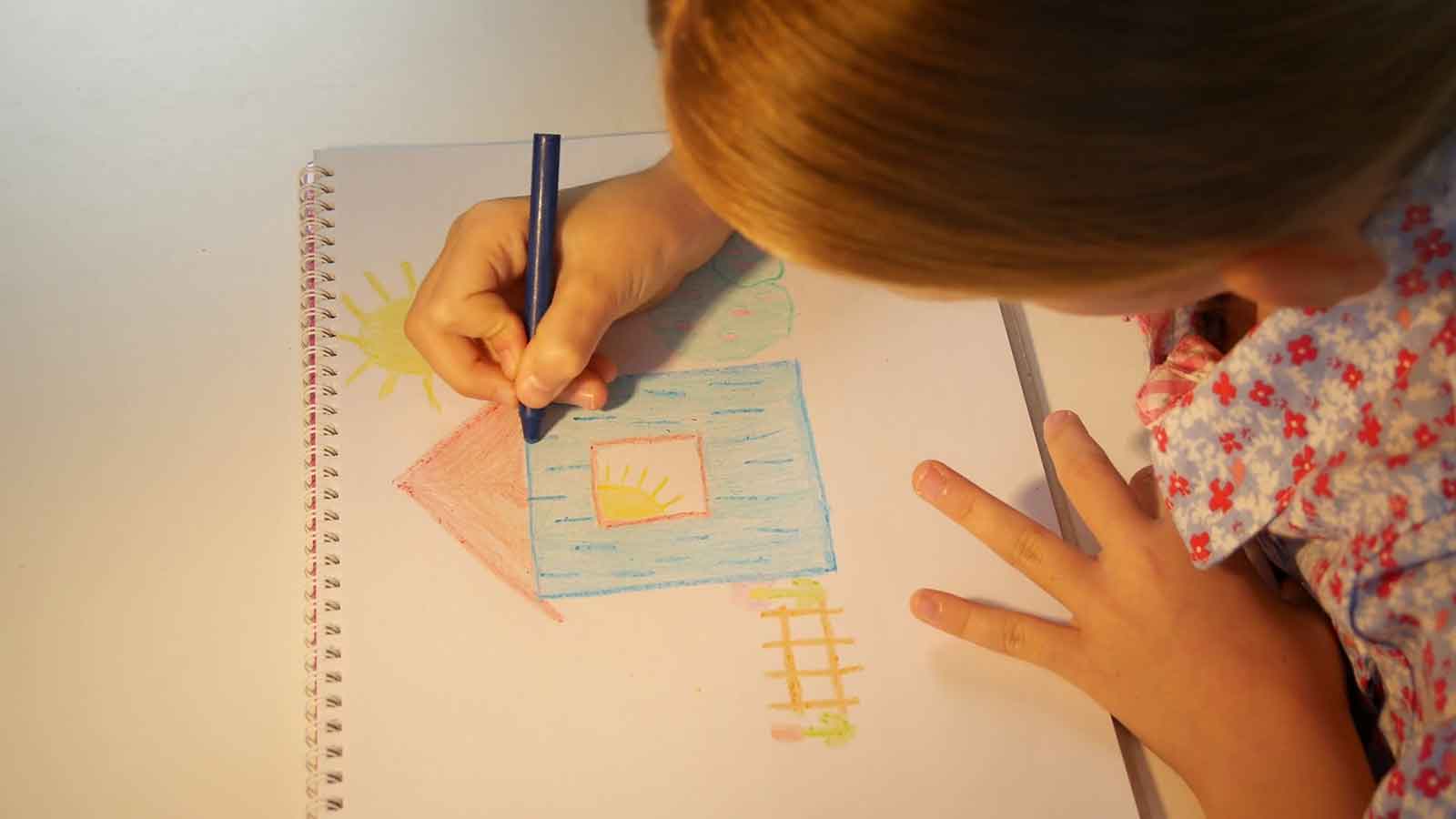 A young girl drawing a colourful house in a note book