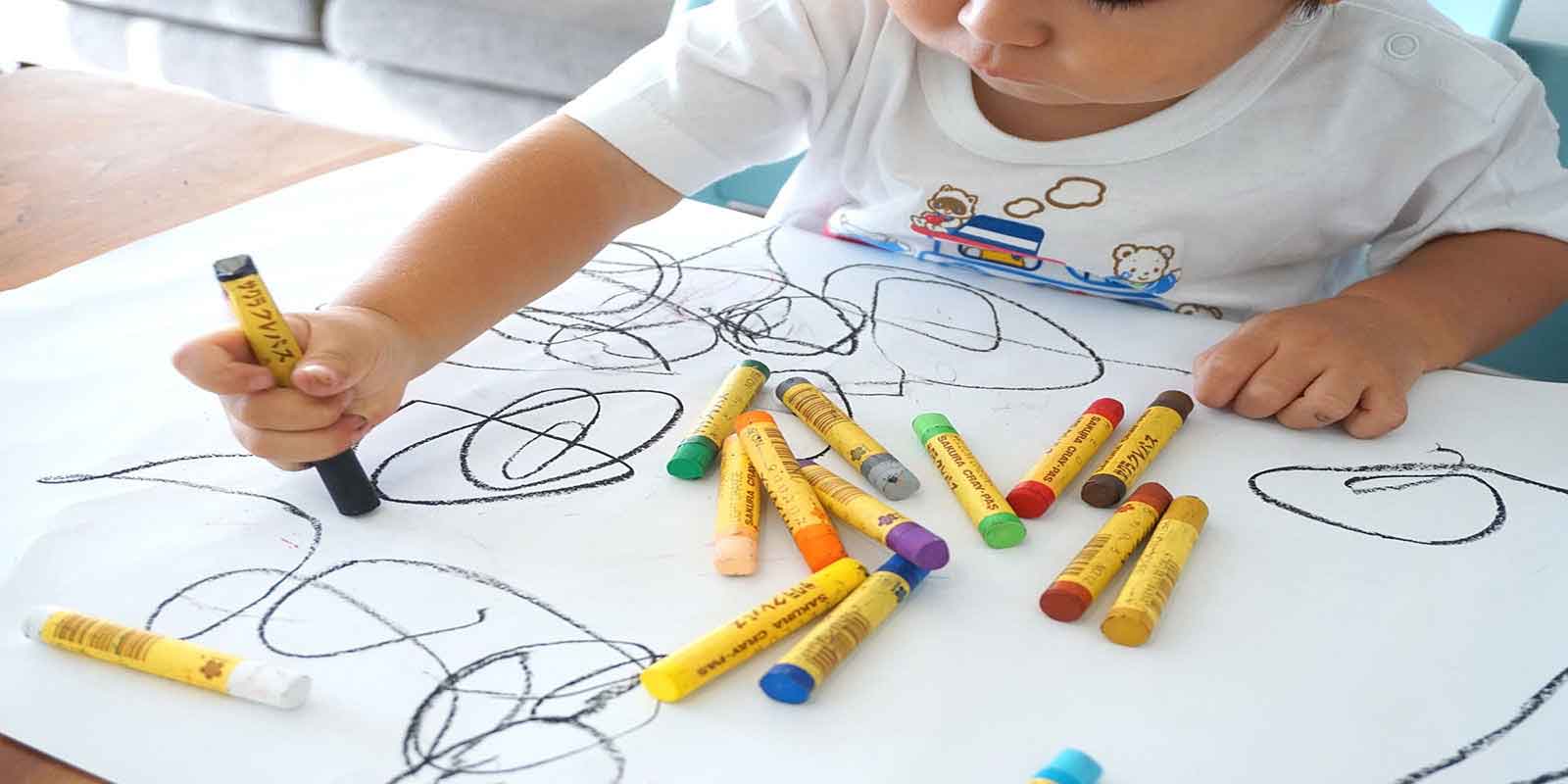 A young child is using crayons to improve fine motor skills