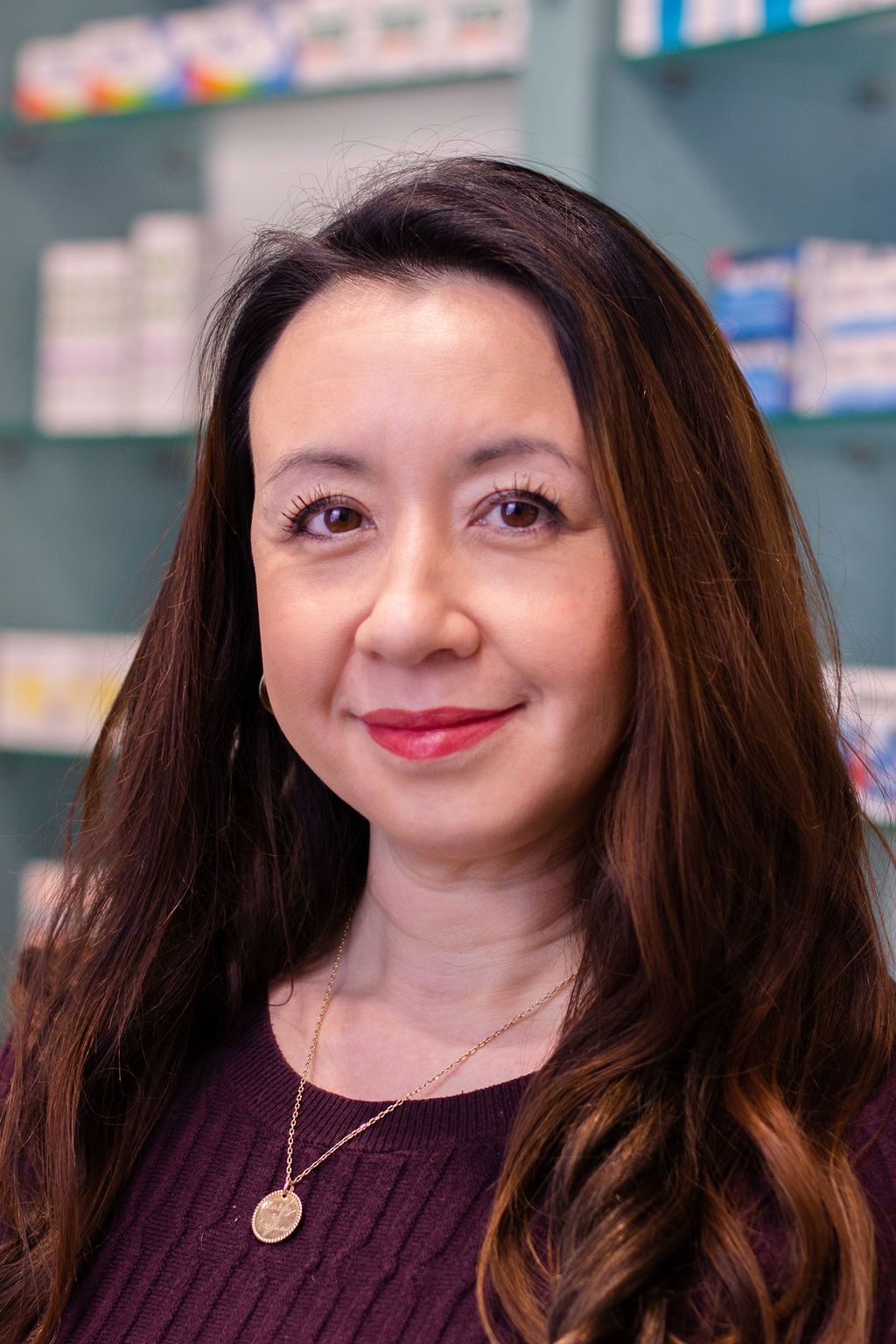 Eine Frau in einem lila Pullover lächelt vor einer Apotheke.