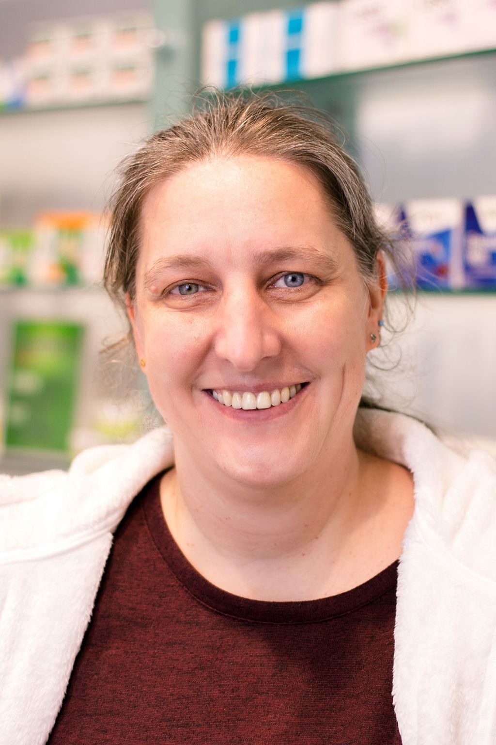 Eine Frau lächelt vor einem Regal in einer Apotheke.