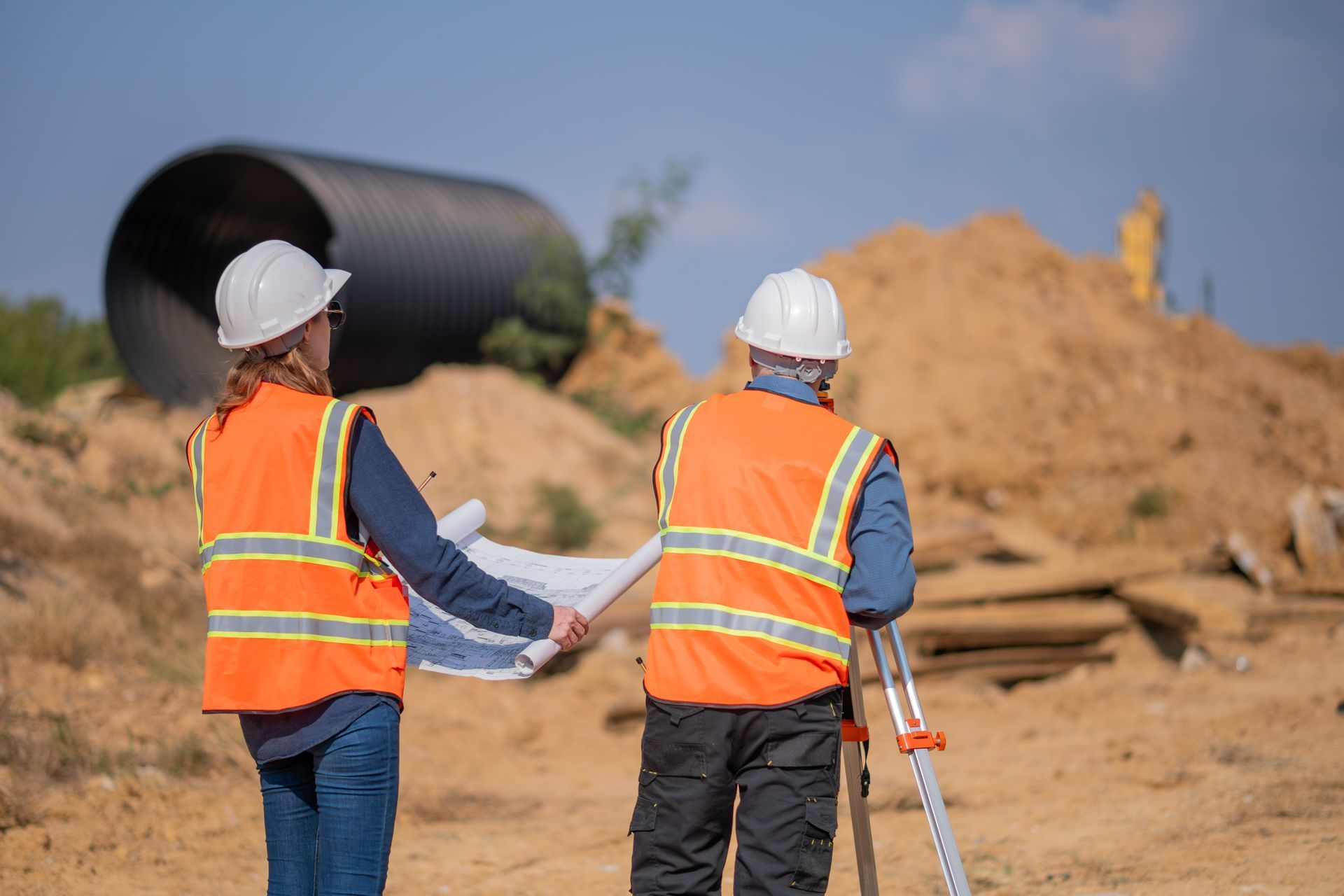 A man and a woman are standing on a construction site looking at a blueprint.