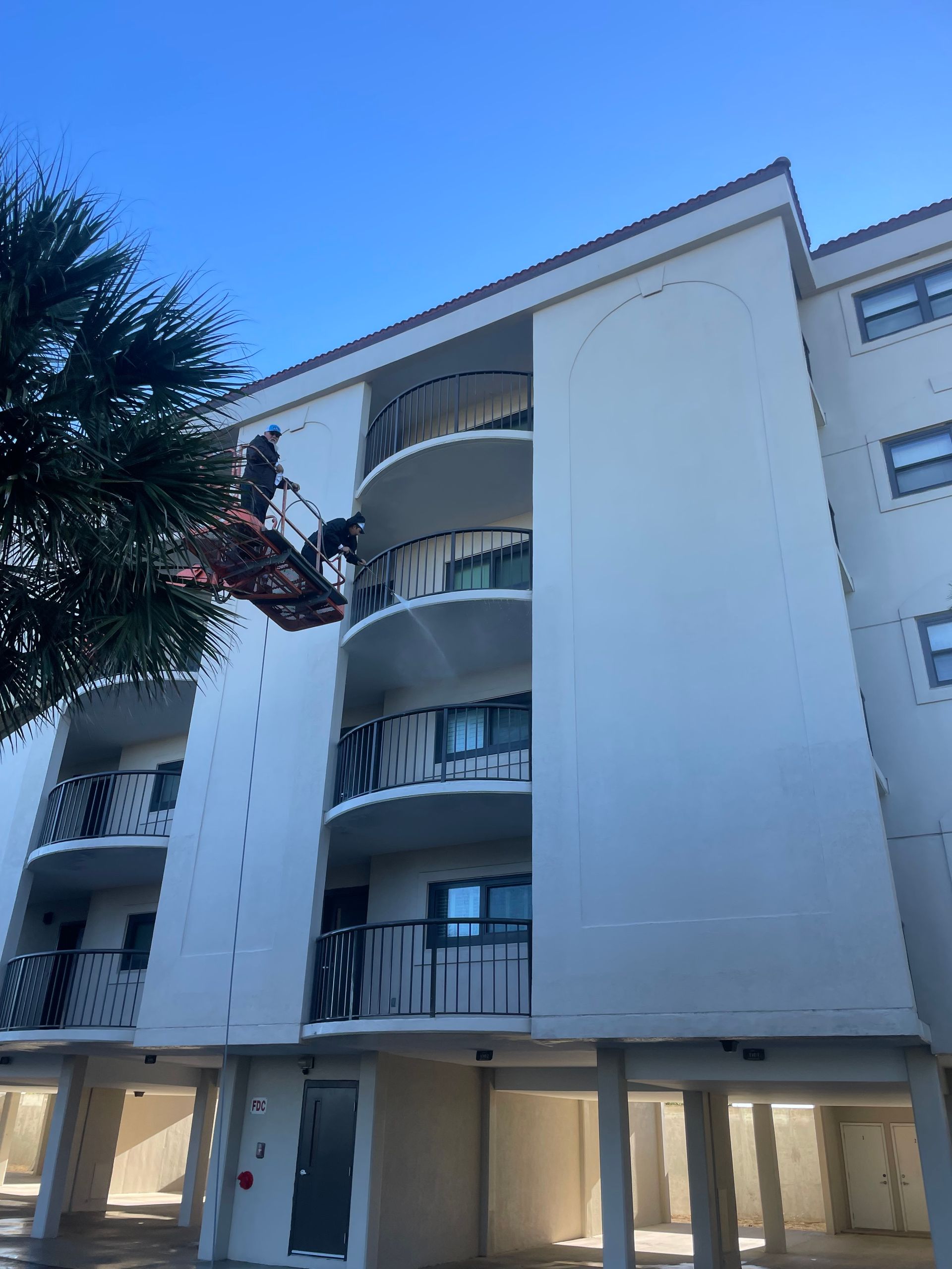 A Man Is Cleaning The Side Of A Building With A Crane — Leland, NC — Coastal Exterior Solutions