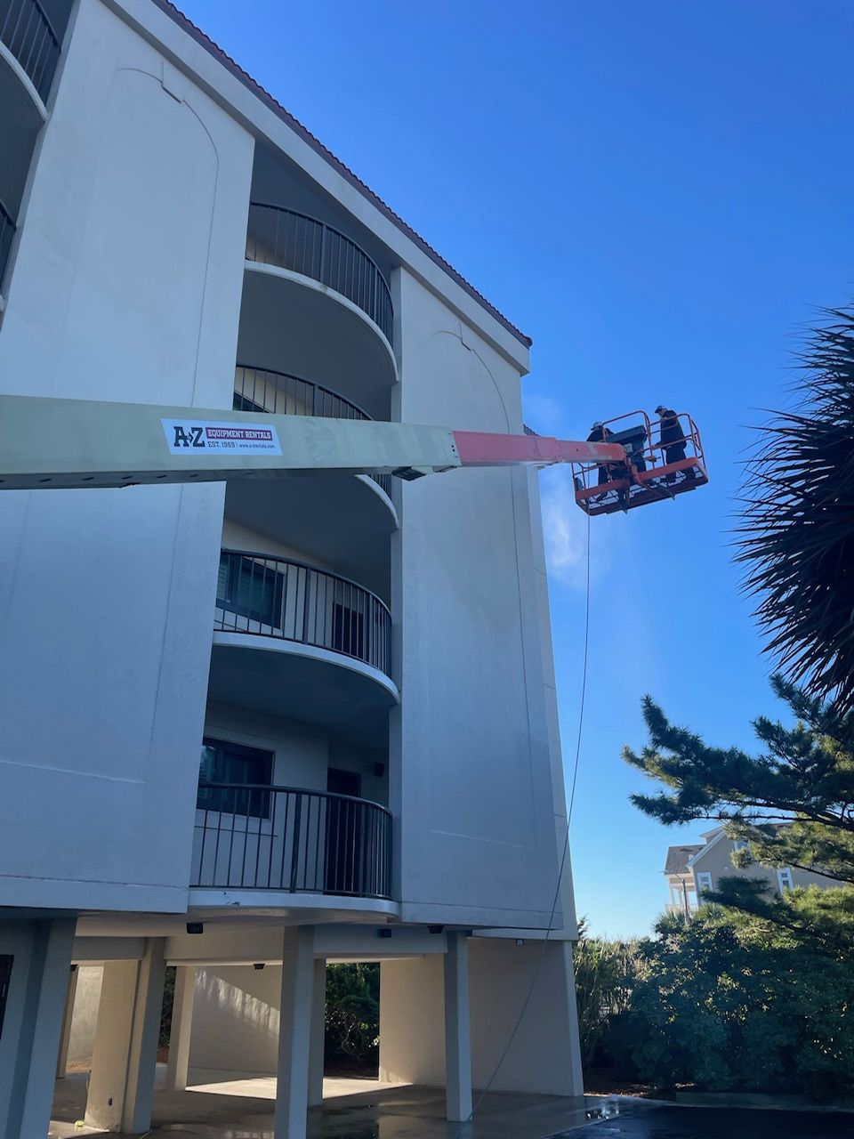A Man Is Cleaning The Side Of A Building With A Crane With A Tree — Leland, NC — Coastal Exterior Solutions