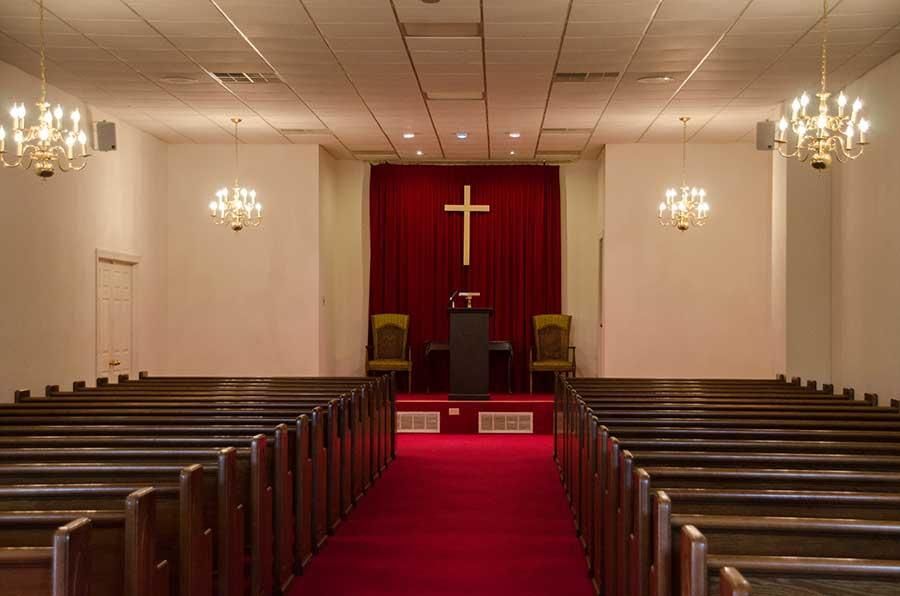 An empty church sanctuary with rows of pews facing a red carpet, altar, and cross.