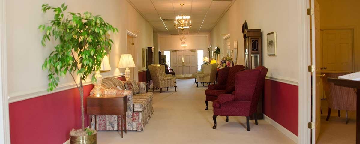 Interior hallway with red-trimmed walls, seating areas, a large plant, and doorway.