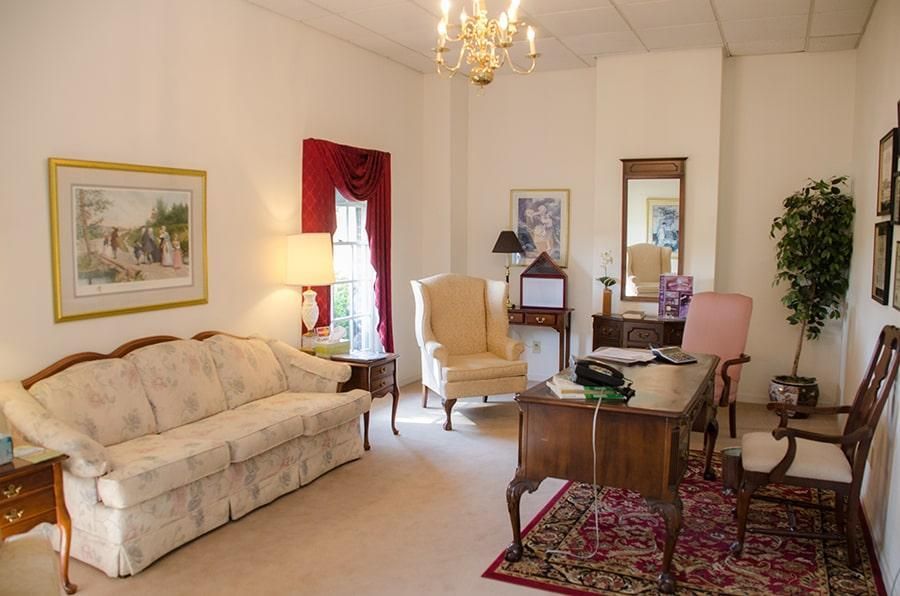 Cozy office with a floral sofa, ornate desk, chandelier, and red rug.