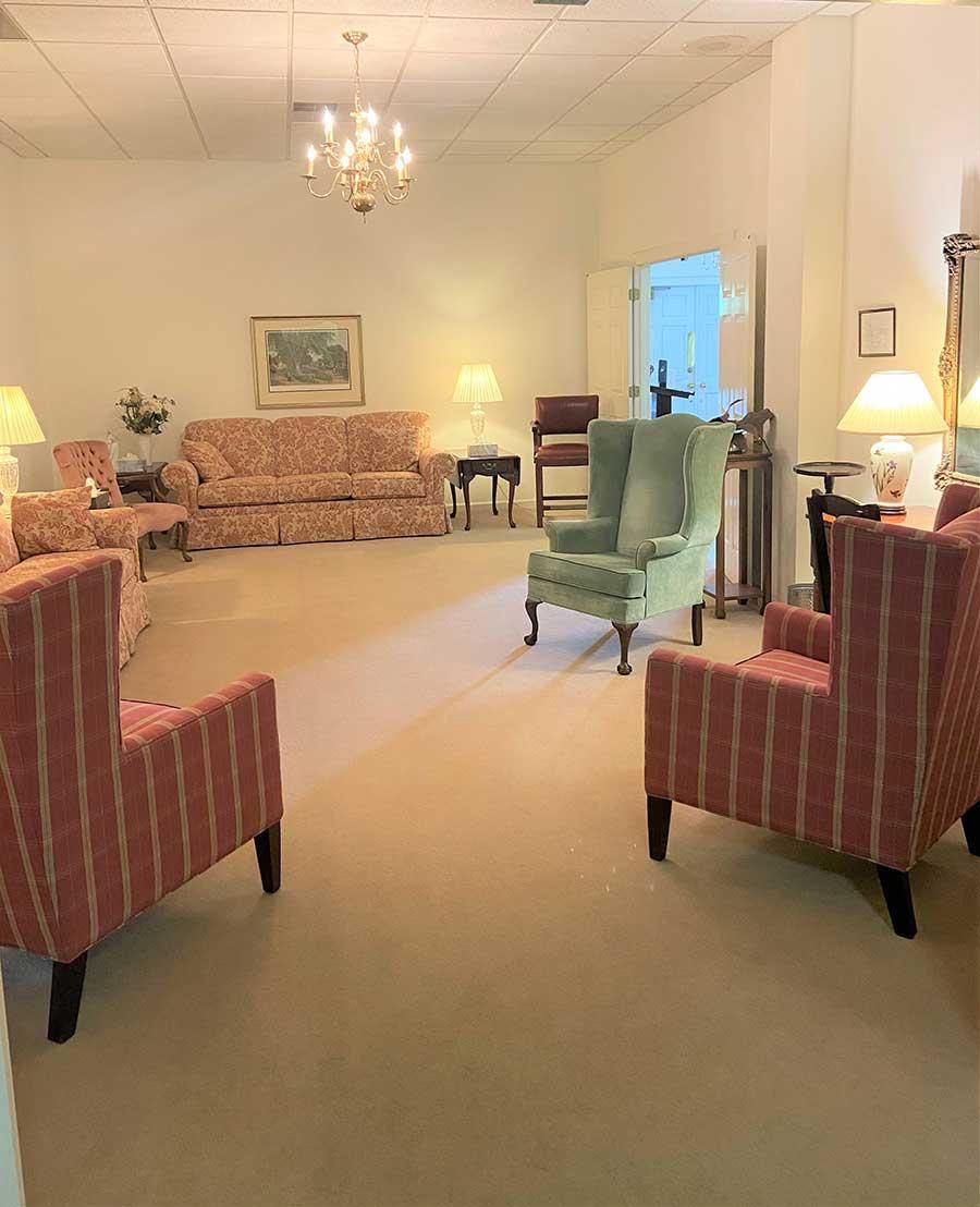 Lounge area with pink and green chairs, floral couch, and chandelier in a softly lit room.