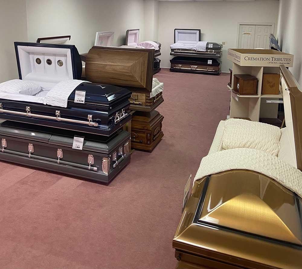 Funeral home showroom with multiple open and closed coffins on display.