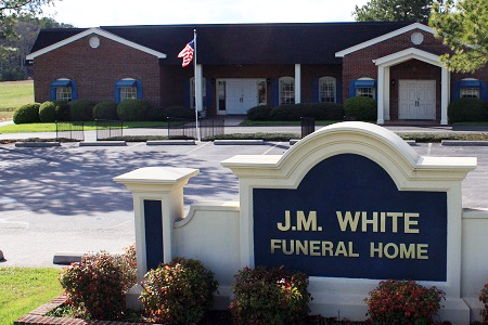 White building with American flag, front porch, green trim, and lawn.