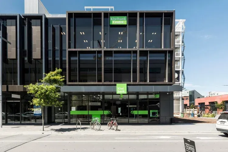 Modern office building with dark glass and green accents, bicycles parked out front.