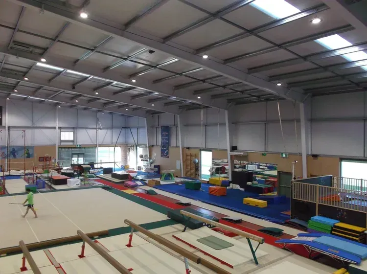 Gymnasium interior with gymnastic equipment, large open space. A child walks across floor.