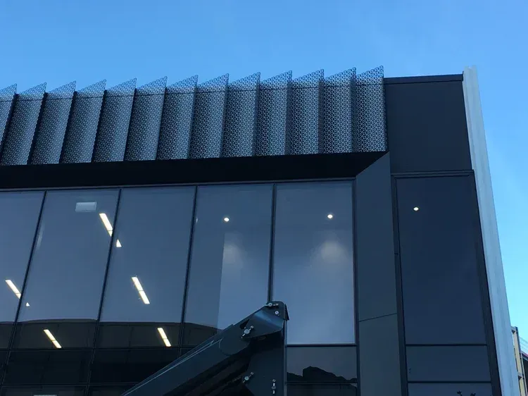Black commercial building with glass windows and patterned metal overhang against a clear blue sky.