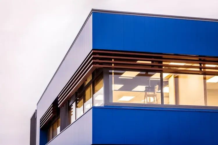Blue and white building corner with wood slat accents over windows, looking up.