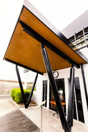 Modern building entrance with angled black support beams and wooden ceiling.